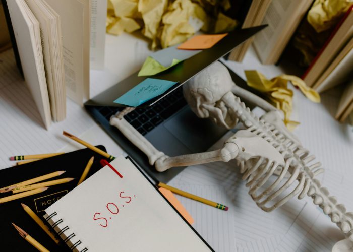Dramatic still life of a skeleton overwhelmed at an untidy office desk with S.O.S. note.
